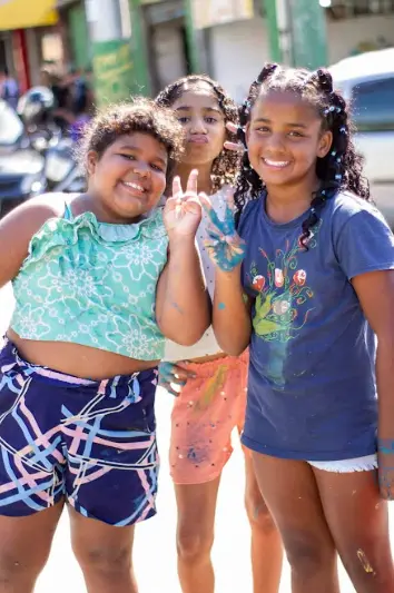 Três crianças participantes do projeto sorrindo para  a câmera.